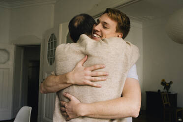 Happy man embracing parent while standing at home - MASF34761