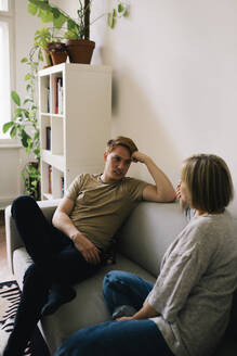 Mann im Gespräch mit einem Elternteil, während er zu Hause auf dem Sofa sitzt - MASF34764