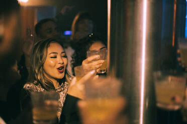 Glückliche junge Frau mit einem Getränk in der Hand, die mit Freunden in einem Nachtclub tanzt - MASF34780