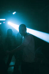 Young man dancing against illuminated spotlight at nightclub - MASF34799