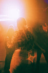 Von hinten beleuchtete junge Frau tanzt in beleuchtetem Nachtclub - MASF34803
