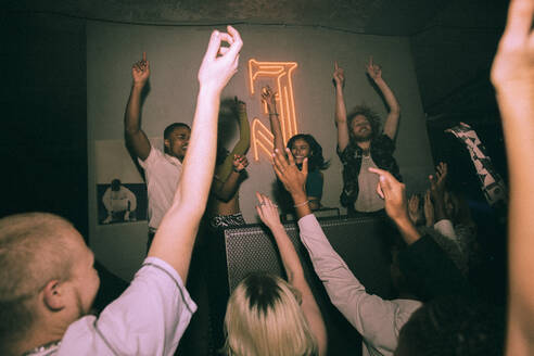 Multirassische junge Männer und Frauen tanzen mit einem weiblichen DJ in einem beleuchteten Nachtclub - MASF34816