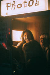 Glückliche junge Frauen, die sich in einem Nachtclub in einer Fotokabine fotografieren lassen - MASF34822