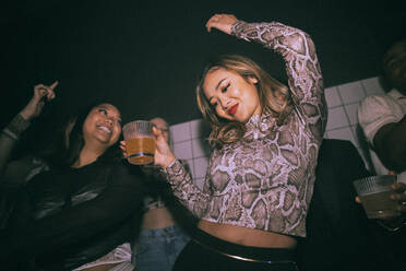 Unbekümmerte junge Frau mit Getränk tanzt mit einer Freundin in einem Nachtclub - MASF34831