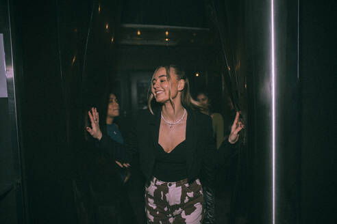 Fröhliche junge Frau, die aus dem Badezimmer kommt, mit Freunden im Hintergrund in einem Nachtclub - MASF34836