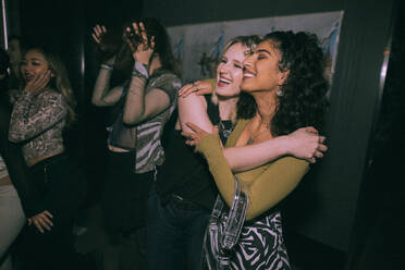 Fröhliche junge Frauen umarmen sich in einem Nachtclub - MASF34838