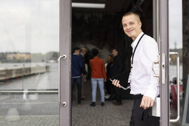 Porträt eines lächelnden jungen Geschäftsmannes, der am Eingang eines Kongresszentrums steht - MASF34850