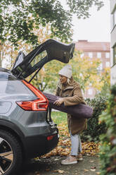 Reife Frau lädt Teppich in den Kofferraum eines Autos - MASF34900