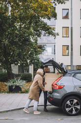 Älteres Paar, das während eines Umzugs gemeinsam Karton in den Kofferraum eines Autos lädt - MASF34907