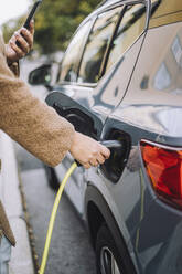 Hand einer Frau, die ein Ladegerät für ein Elektroauto an einer Station anschließt - MASF34917