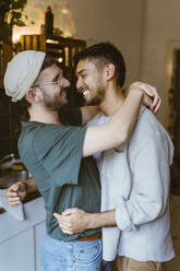 Seitenansicht eines glücklichen schwulen Paares, das sich in der Küche zu Hause umarmt - MASF34937