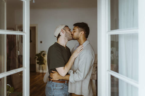 Side view of romantic gay couple kissing each other seen through doorway - MASF34943
