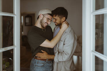 Liebendes homosexuelles Paar, das zu Hause lächelnd beieinander steht - MASF34944