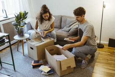 Boyfriend and girlfriend talking to each other while unboxing cardboard boxes in living room at home - MASF34957