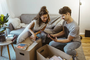 Man sharing photo frame with girlfriend while unboxing cardboard boxes at home - MASF34958