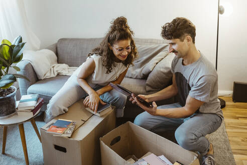 Mann teilt Fotorahmen mit Freundin beim Auspacken von Kartons zu Hause - MASF34958