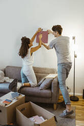 Couple helping each other while mounting photo frame on wall at home - MASF34960