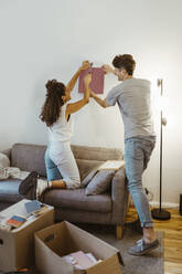 Ein Paar hilft sich gegenseitig bei der Montage eines Fotorahmens an der Wand zu Hause - MASF34960