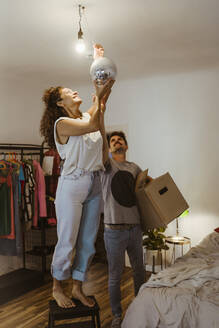 Mann hilft seiner Freundin bei der Installation einer Discokugel mit beleuchteter Glühbirne zu Hause - MASF34968