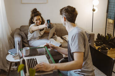 Glückliche Freundin zeigt ihrem Freund das Smartphone mit dem Laptop zu Hause - MASF34971
