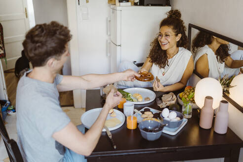 Glückliches Paar, das sich am Esstisch zu Hause das Essen teilt - MASF34976
