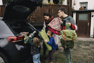 Aufgeregte Familie lädt Picknick-Sachen in den Kofferraum eines Elektroautos vor dem Haus - MASF34985
