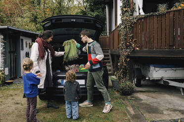 Familie bereitet sich auf ein Picknick vor, während sie Sachen in den Kofferraum eines Elektroautos lädt - MASF34986