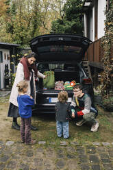 Vater und Mutter im Gespräch mit Kindern in der Nähe eines Elektroautos vor dem Haus - MASF34987