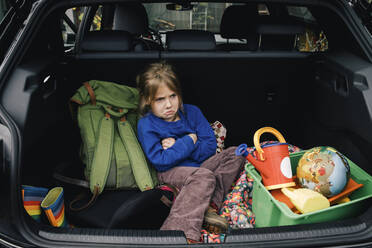 Wütendes Mädchen mit verschränkten Armen sitzt im Kofferraum eines Elektroautos - MASF34992