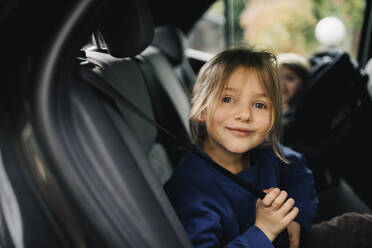 Porträt eines lächelnden Mädchens, das den Sicherheitsgurt hält, während es im Auto sitzt - MASF34993