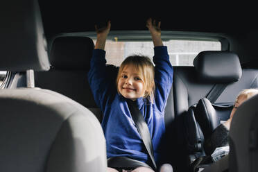 Portrait of smiling girl with arms raised sitting at back seat in car - MASF34995