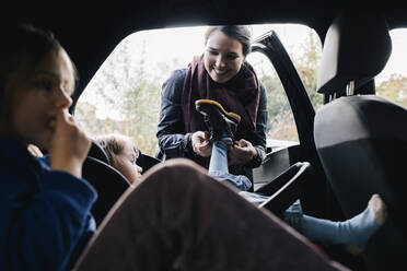 Lächelnde Mutter hilft ihrer Tochter, den Stiefel im Auto anzuziehen - MASF34999