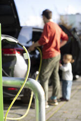Eingestecktes Kabel an einer Station mit einem Mann, der ein Elektroauto auflädt, im Hintergrund - MASF35009