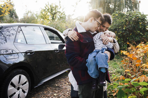 Vater und Mutter spielen mit ihrer Tochter bei einem Picknick in der Nähe eines Elektroautos - MASF35012