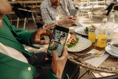 Mann fotografiert Essen auf dem Tisch mit seinem Smartphone in einem Straßencafé - MASF35044