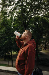 Seitenansicht eines übergewichtigen Mannes, der Wasser aus einem Trinkbecher trinkt - MASF35061
