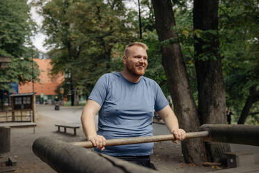 Lächelnder übergewichtiger Mann, der im Stehen im Park trainiert - MASF35065