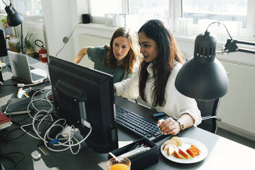 Weibliche Geschäftskollegen teilen sich einen Desktop-PC am Schreibtisch, während sie im Büro arbeiten - MASF35082