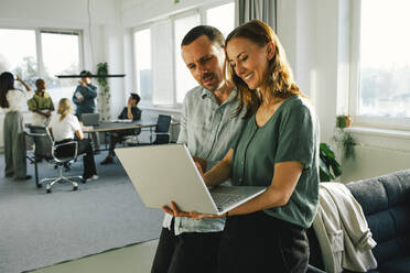 Male and female business professionals discussing over laptop at office - MASF35098