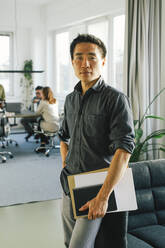 Porträt eines selbstbewussten Geschäftsmannes, der ein Dokument hält, während er im Büro steht - MASF35099