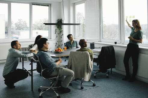 Geschäftsfrau bei einer Besprechung mit Kollegen, die am Schreibtisch im Büro sitzen - MASF35123