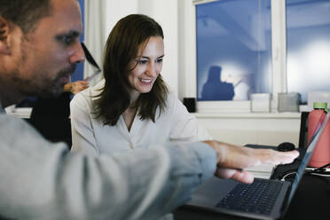 Lächelnde Geschäftsfrau, die mit einem männlichen Kollegen im Büro am Laptop arbeitet - MASF35133