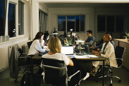 Business colleagues working late while sitting at desk in office - MASF35135