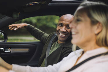 Happy bald man looking at woman driving car - MASF35138