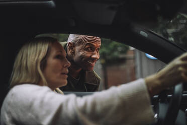 Smiling man looking away while talking to woman sitting in car - MASF35139