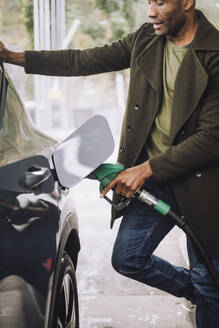 Älterer Mann, der an einer Tankstelle steht und Benzin ins Auto pumpt - MASF35144