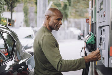 Seitenansicht eines reifen Mannes beim Bezahlen mit Kreditkarte an einer Tankstelle - MASF35150