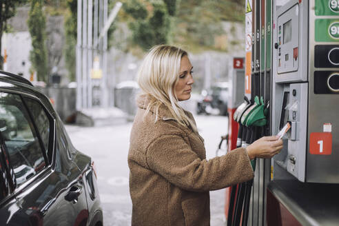 Reife Frau beim Bezahlen mit Kreditkarte an einer Tankstelle - MASF35151