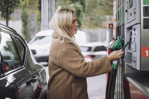 Seitenansicht einer blonden Frau, die mit ihrem Smartphone an einer Tankstelle bezahlt - MASF35152