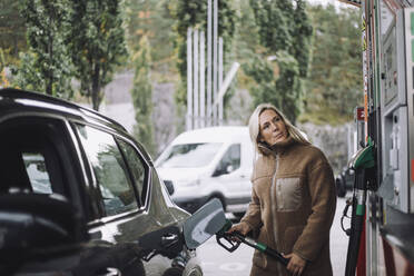 Reife Frau beim Tanken im Auto, während sie an der Tankstelle steht - MASF35154